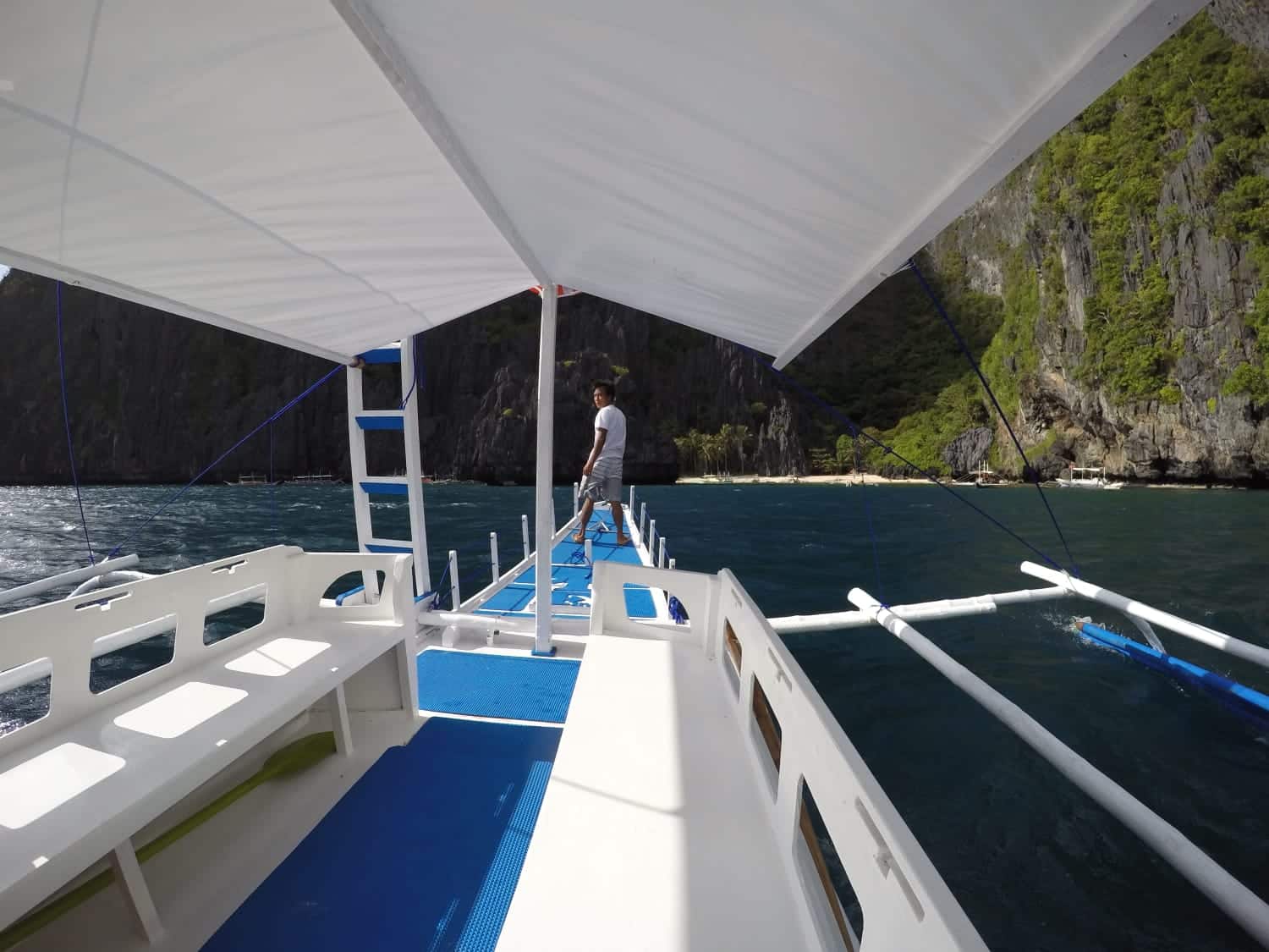 Boat crew member on the deck of an island-hopping bangka among limestone cliffs in Palawan