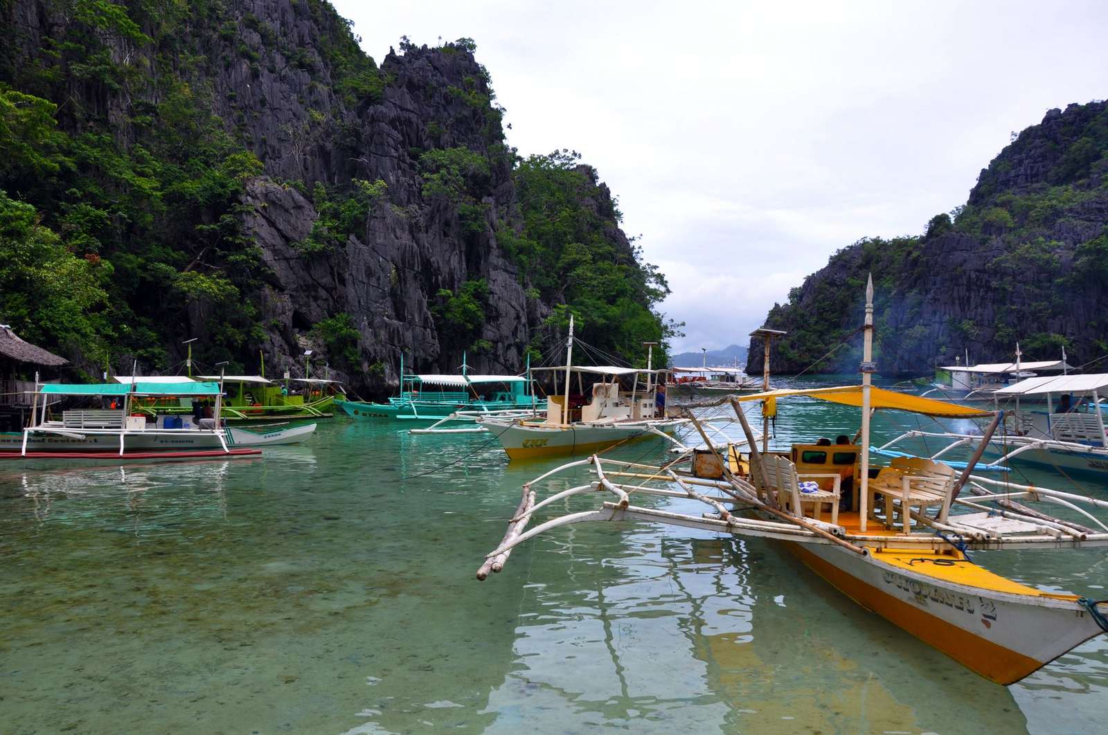 Traditional outrigger boats in clear water below cliffs in El Nido, Palawan