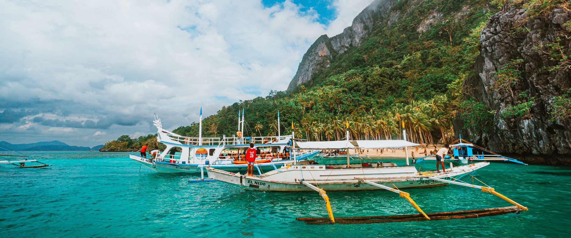 Outrigger boats on turquoise water below cliffs in El Nido, Palawan